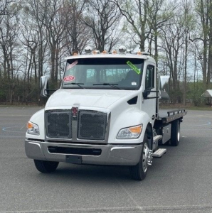 Kenworth T270/T680-style white tow truck front view showing grille, headlights, and cab with orange clearance lights. Flatbed visible in background.