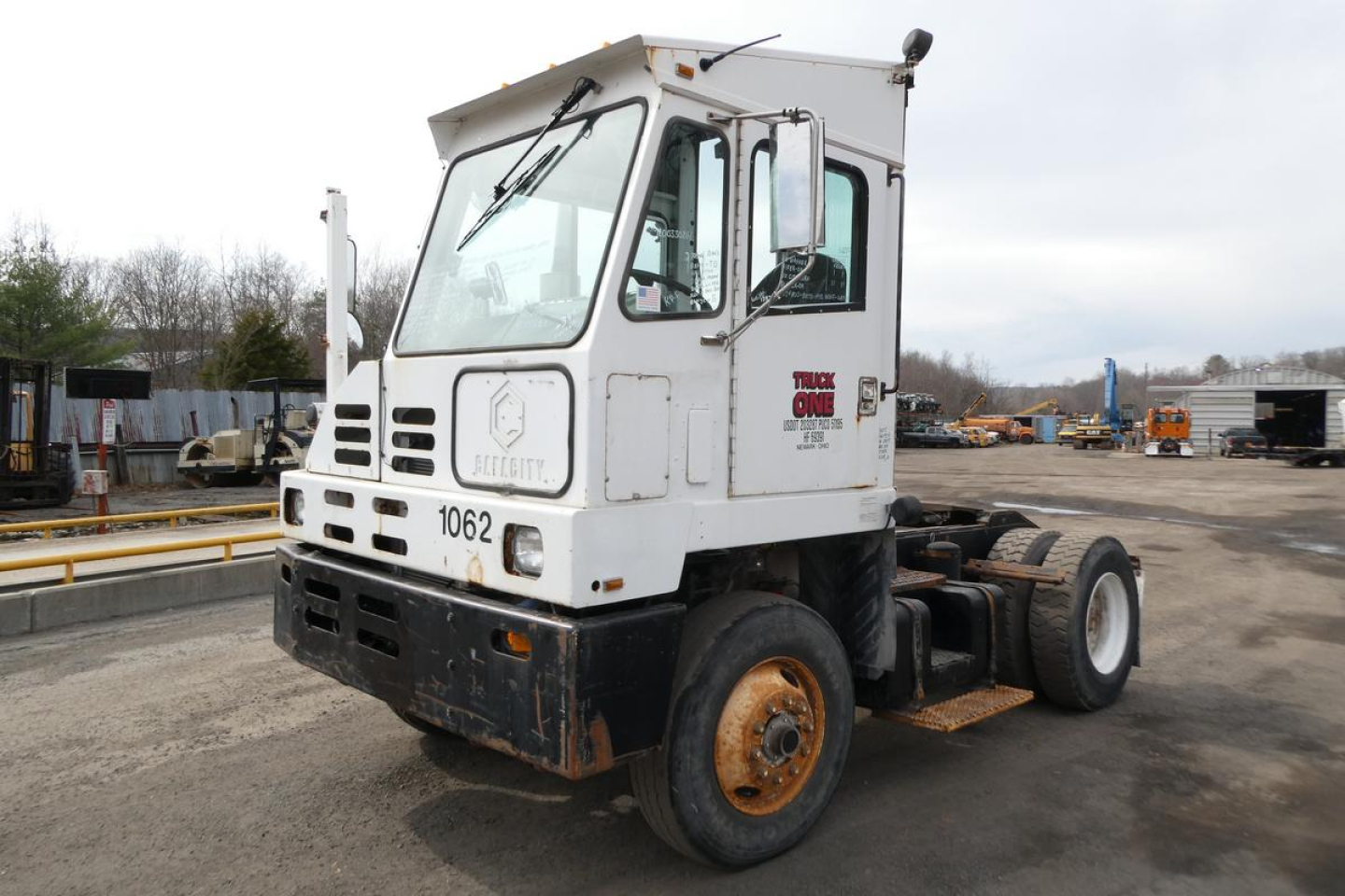 Truck cab showing TJ5000 chassis, white cab with black bumper, faded decals, and large front windshield; wheel rims and chassis exposed.