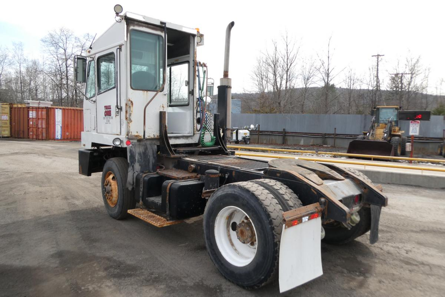 Truck chassis with TJ5000 configuration showing rear wheels and cab, grime on tires and frame, front cab window.