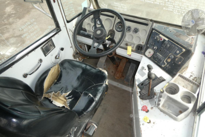 Truck cab interior with steering wheel, dashboard gauges, and torn driver's seat.