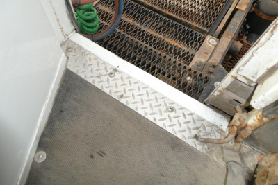Trucks equipment area showing diamond plate floor and metal mesh grate with rusted latch and green hose in background
