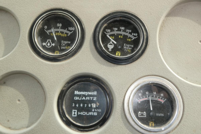 Dashboard gauges including two engine temperature/pressure gauges, a Honeywell quartz hour meter, and a volts gauge. Circular dials with black faces, white markings, yellow indicators.