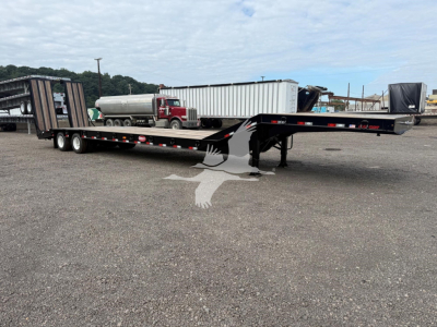 Trailer showing lowboy/drop deck trailer with black steel frame and dual rear axles, side rails, and gooseneck area visible.