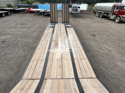 Flatbed trailer deck showing wooden planks and black steel supports for a Dorsey LB35-33CS model, viewed from the rear toward the hitch area with trucks in a yard.