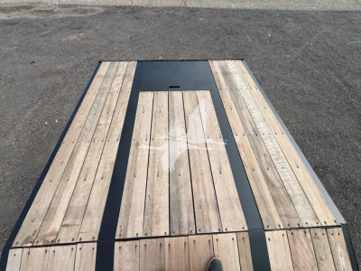 Trailer bed showing wooden deck planks with a central dark metal panel and a small access hatch, viewed from above.