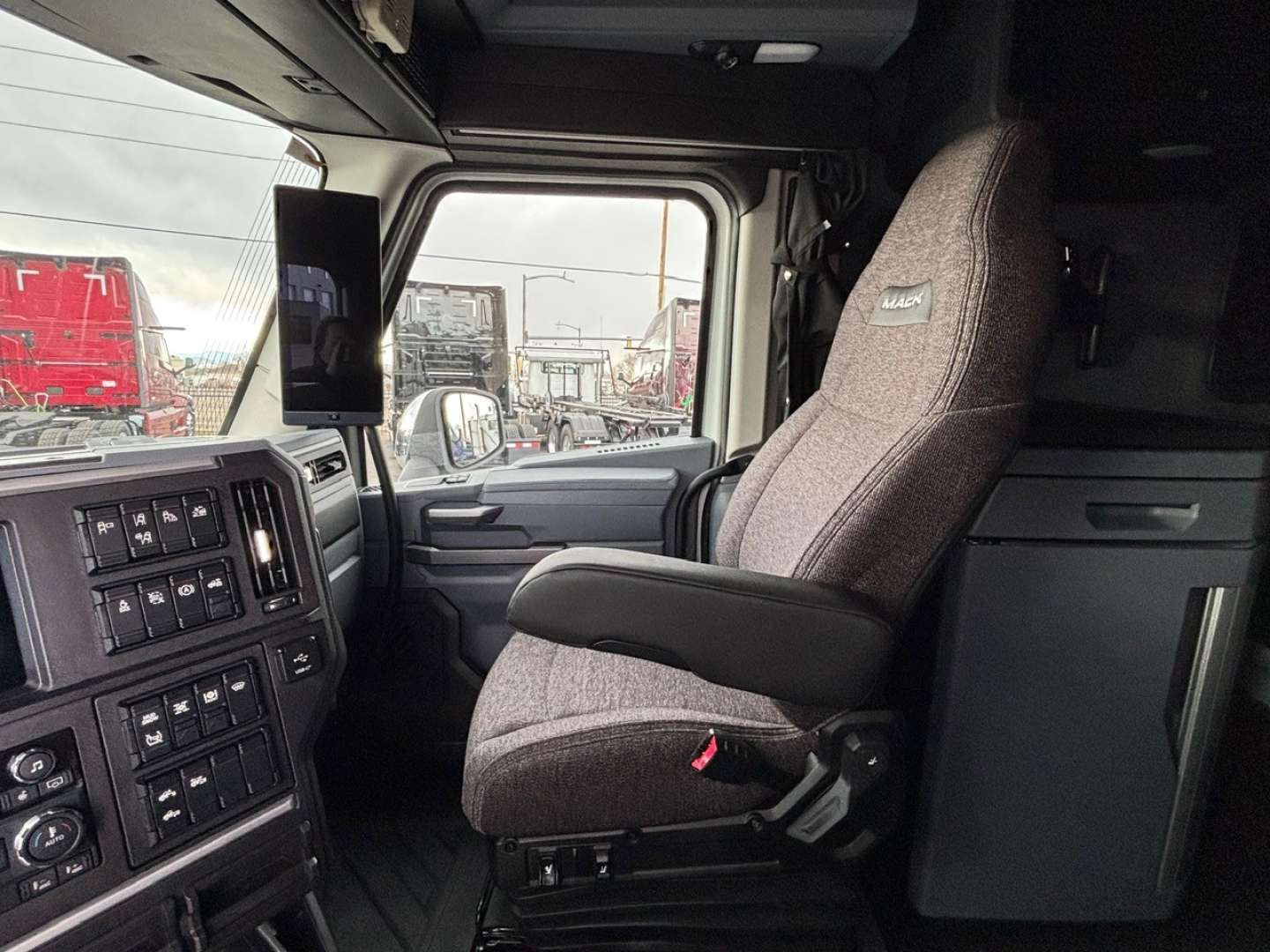 Truck cab interior with driver seat and dashboard of a 2026 Mack PR64T76H tractor showing steering wheel, controls, and side window.
