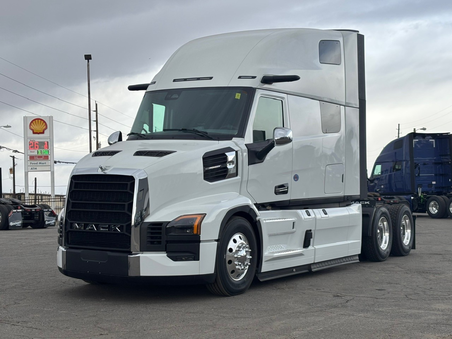 Mack PR64T76H conventional sleeper tractor in light gray, front-left view showing cab with large windshield, integrated air intake, and dual rear axles.