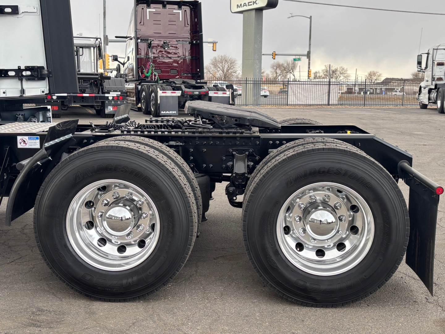 Dual rear axles of a Mack PR64T76H truck chassis showing chrome wheels and tires, frame, and fifth wheel; no cab visible.