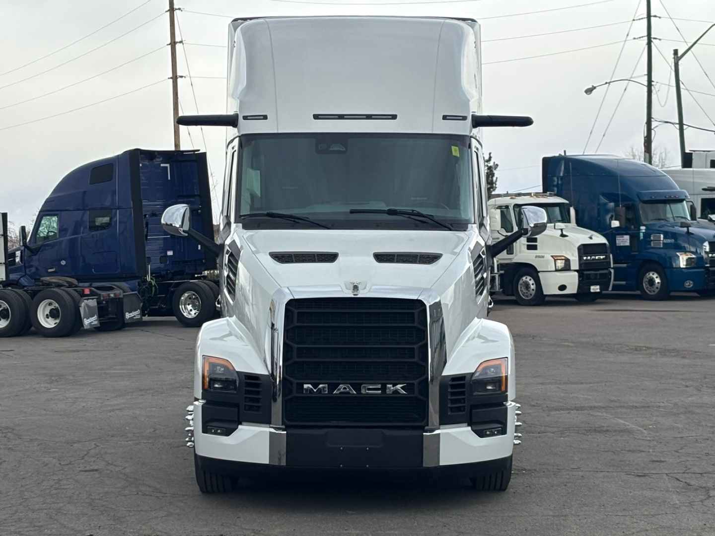 Truck front view showing Mack PR64T76H cab-over-engine with white exterior and black grille, daytime.