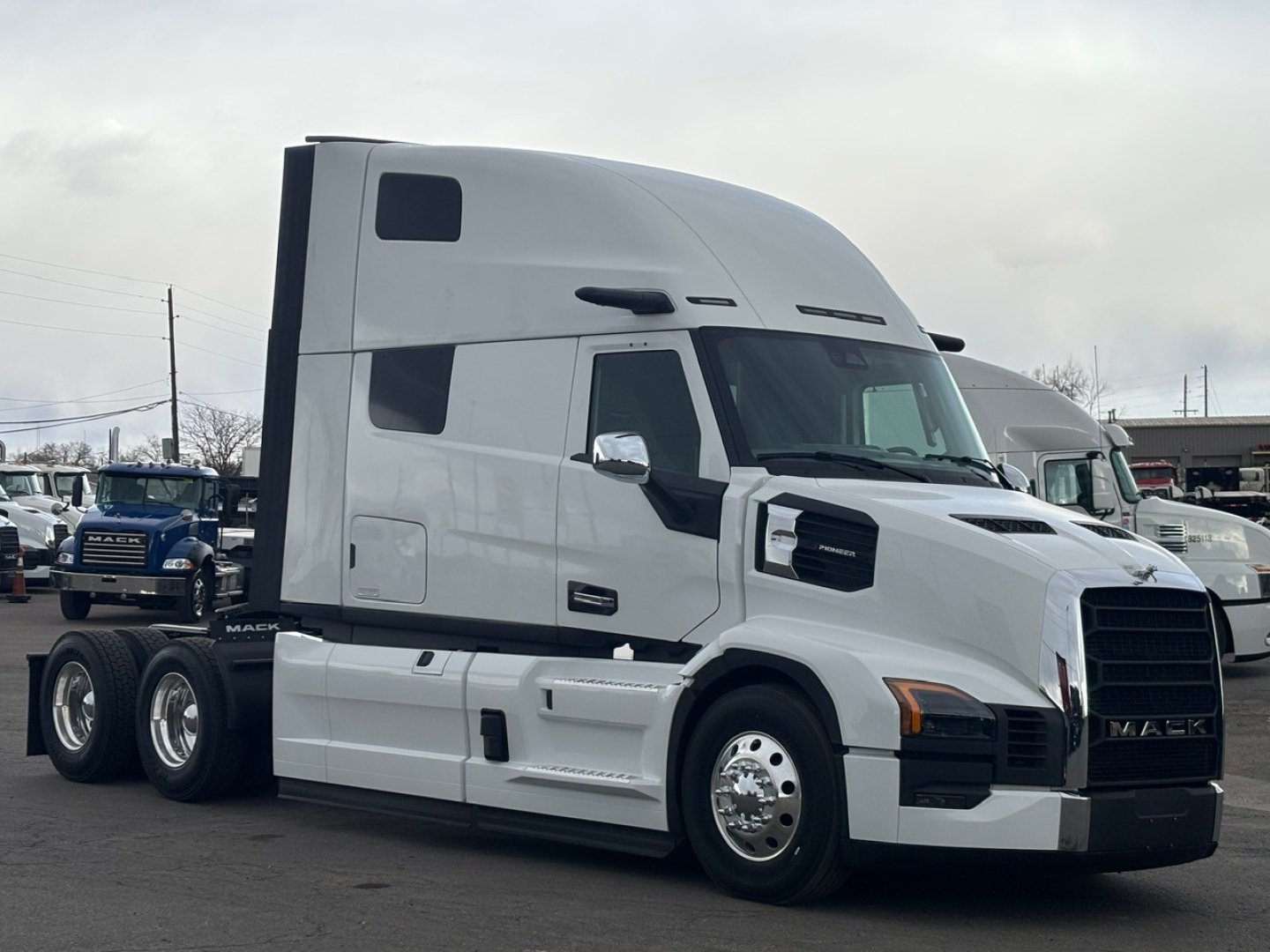 Semi truck tractor in white, side view with sleeper cab and black grille. Visible text includes Mack logo on grille and windowed cab.