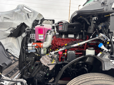 Truck engine bay showing red engine block, pink coolant reservoir, and various hoses and components.
