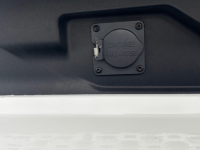 Engine heater cap with latch shown on a Mack truck engine bay area.