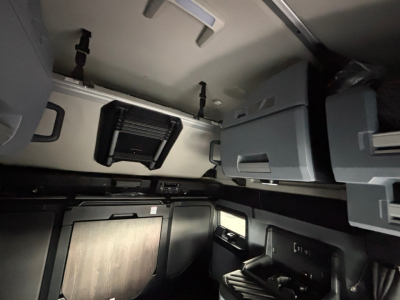 Cab interior showing overhead storage bins and cabinets inside a Mack PR64T76H sleeper, with a small vent/air unit and multiple compartments.