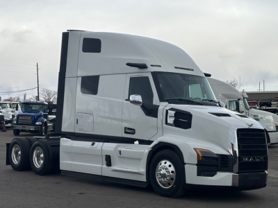Semi truck tractor in white, side view with sleeper cab and black grille. Visible text includes Mack logo on grille and windowed cab.