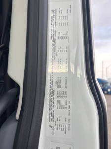 VIN sticker and specification label on Mack PR64T76H truck door jamb showing model, VIN 1M1PR4GY6TM101015, stock 71642, category conventional sleeper, new unit, with engine and axle data in small print.