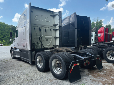 Truck tractor rear three-quarter view showing Sleeper cab with dual rear axles and fifth wheel area, gray color, several other trucks in background.