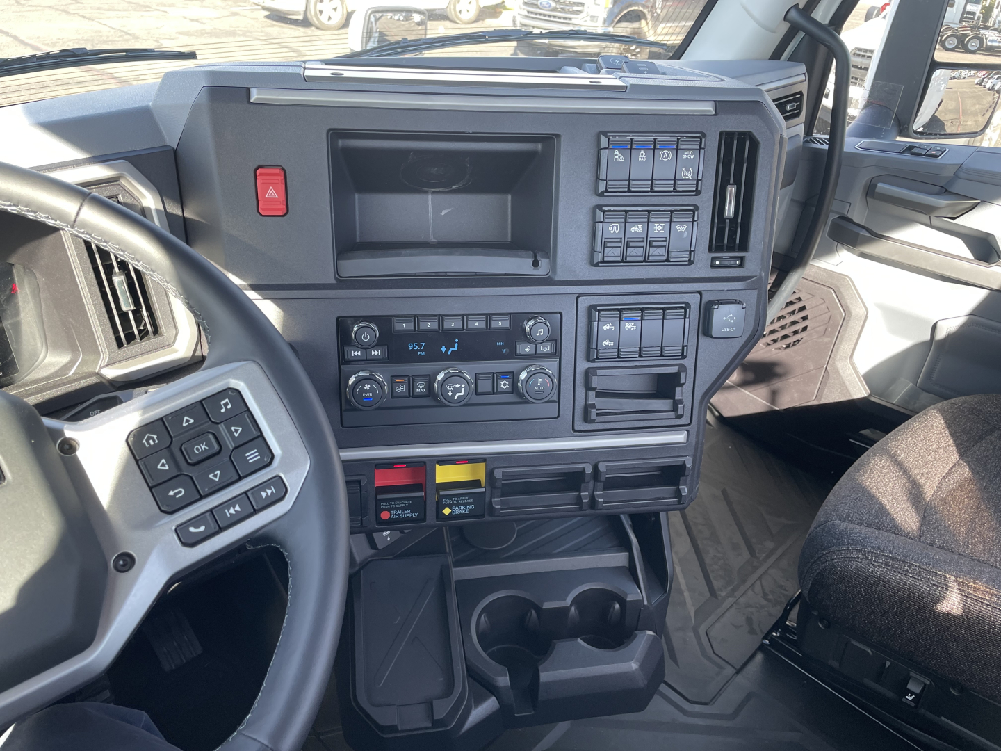 Mack PR64T truck interior dashboard with steering wheel, control panels, climate controls, and storage compartments. visible switches and cup holders.