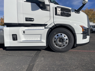Mack PR64T truck left-front section with wheel, fender, and steps visible; white cab and chrome wheel hub; blue sky in background.
