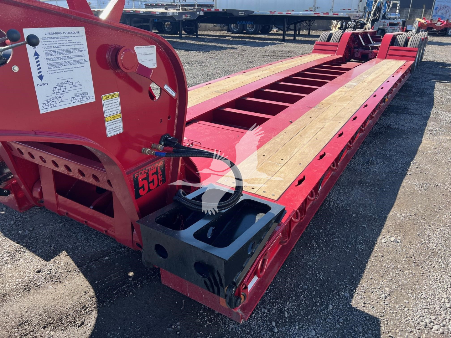 Red Fontaine lowboy trailer chassis showing hydraulic controls and deck with wooden planks; VIN 13NE53300V35A7286 visible on side; rear and spare components in background.