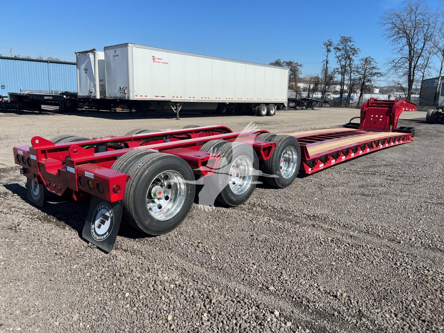 Trailer chassis showing tandem axle configuration with red frame and long flatbed sections in a gravel lot.