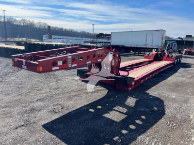 Fontaine lowboy trailer in red with dual axles, showing side rails and gooseneck area; visible labels and reflectors on frame.