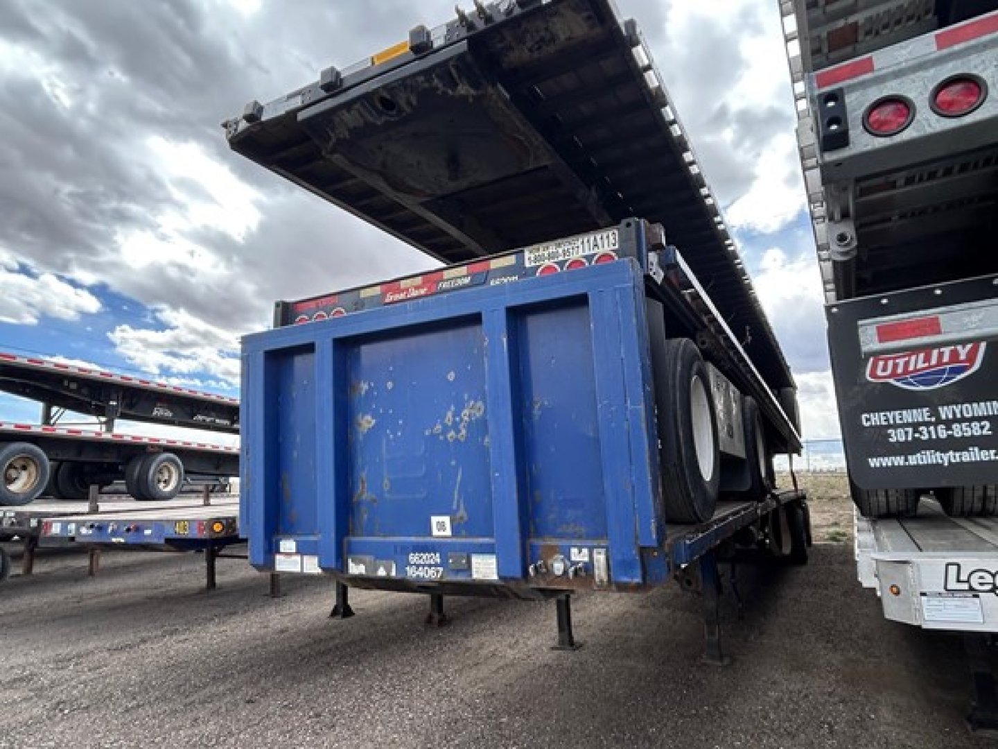 Flatbed trailer in service position with blue steel storage box and raised deck seen from rear side, Great Dane logo and trailer frame visible.