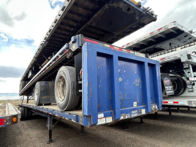 Flatbed trailer with a raised blue steel bed and a spare tire on the side, labeled Great Dane steel spread air, long trailer with wheel and ramps visible.