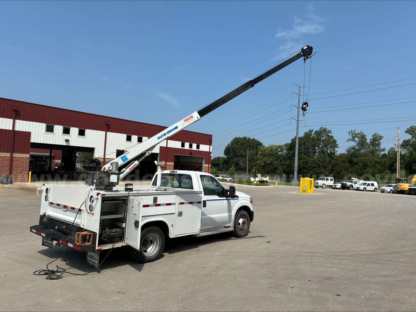 Service/Utility truck with a long crane arm extended from the bed, white damaged-free paint, rear view showing storage compartments and equipment on a parking lot.
