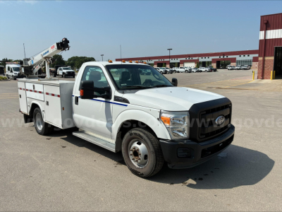 Ford F-350 utility/service body truck with bucket lift viewed from front-left, white cab, black grille, in a parking lot.