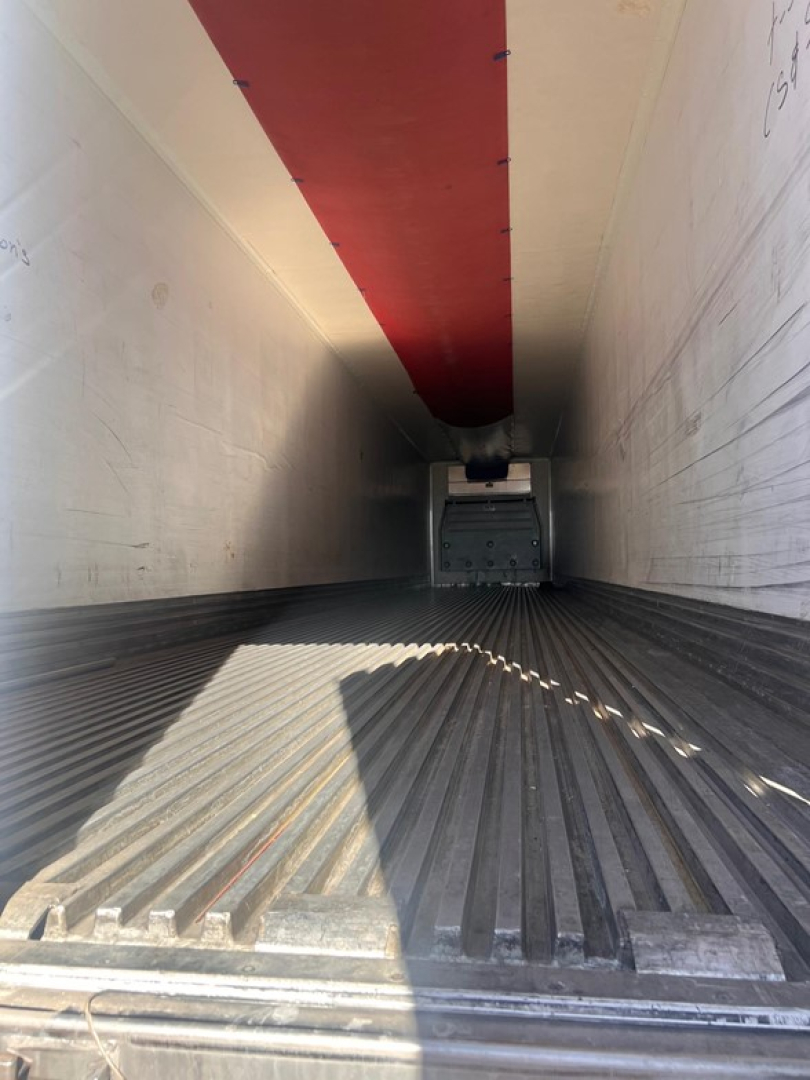 Inside a Great Dane air-ride reefer trailer showing the ribbed metal floor extending toward a swing door at the far end; white interior walls with red ceiling strip; rear door area visible.