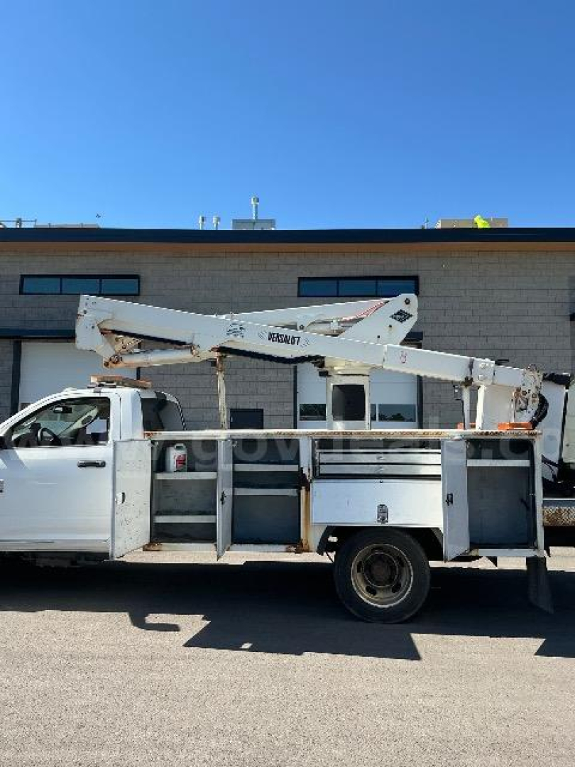Truck bed with mounted bucket lift on a white Dodge Ram 5500 utility body, side view showing tool compartments and crane arm.