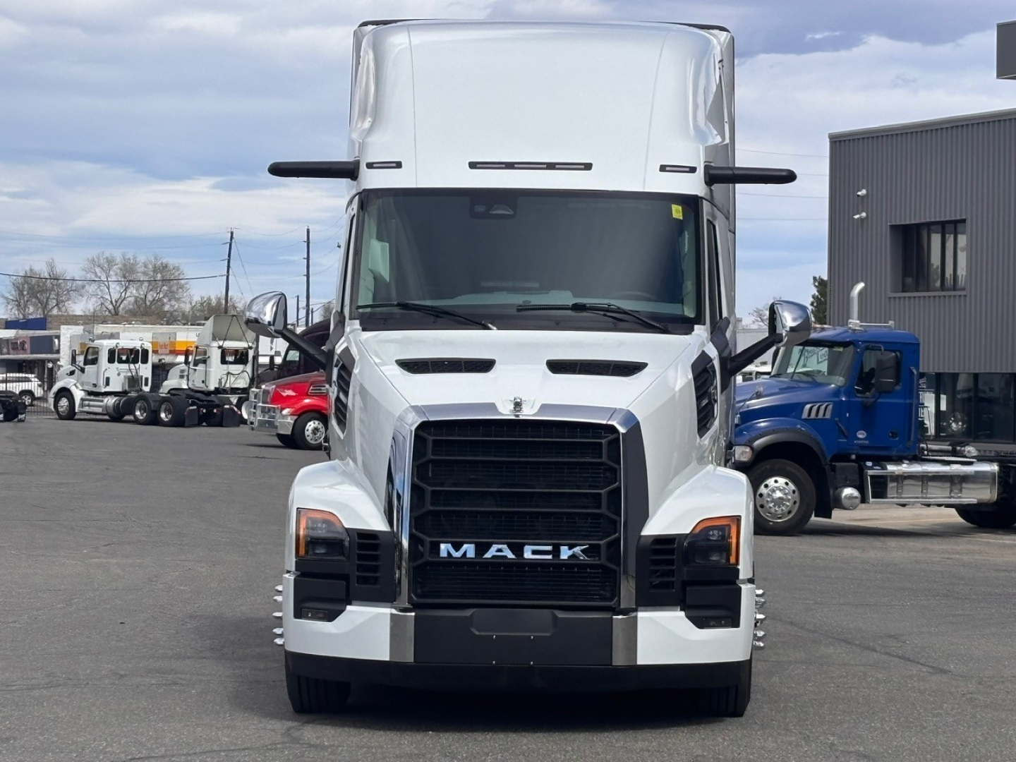 Front view of a white 2026 Mack PR64T76H conventional sleeper truck showing grille with MAC K lettering, large bumper, and side mirrors.