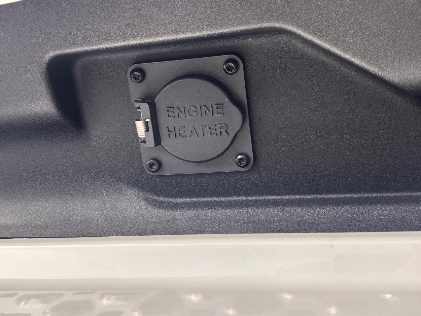 Engine heater cover on Mack truck engine bay with four screws and small lever