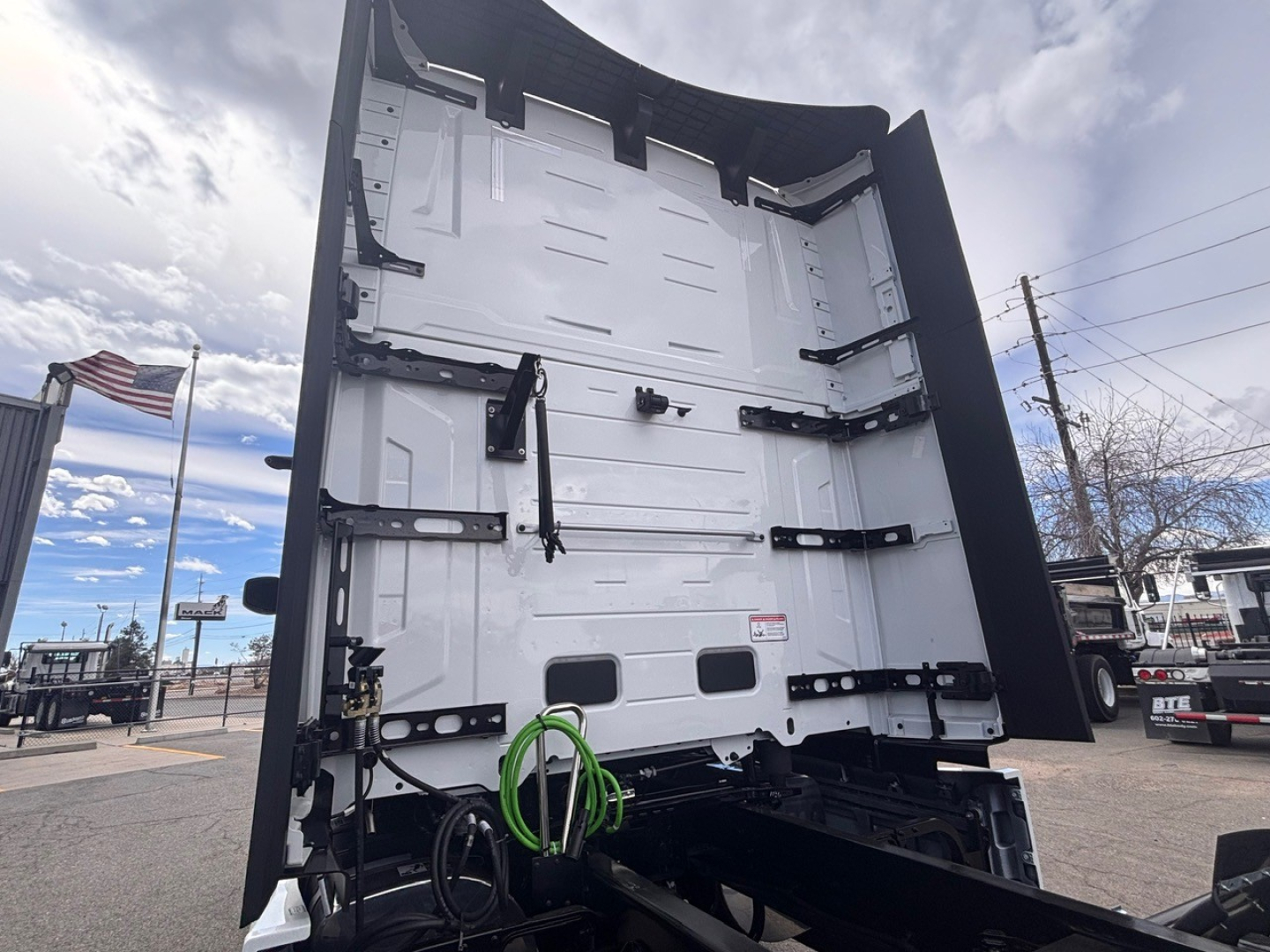Mack PR64T76H truck rear view showing body with green and black hoses/cables, white interior surfaces, and lift gate area.
