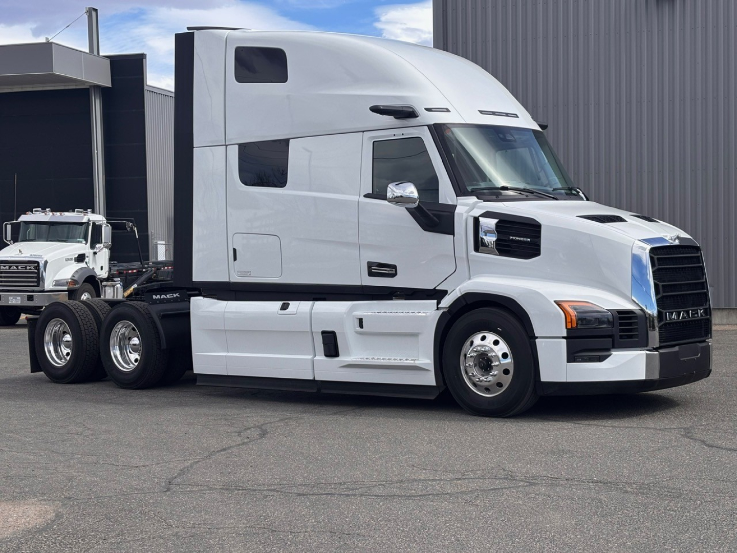 Mack PR64T76H heavy truck in a dealership lot showing side profile of a white sleeper cab with black grille and chrome mirrors.