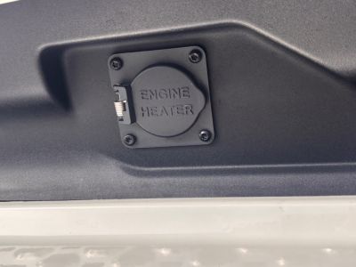 Engine heater cover on Mack truck engine bay with four screws and small lever