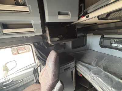 Cab interior of a Mack PR64T76H truck showing overhead cabinetry, sleeper bunk with plastic cover, and front passenger seat in view.