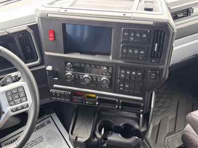 Mack PR64T76H interior dashboard with large central touchscreen, climate controls, and multiple switches; steering wheel visible on left; cup holders and storage below.