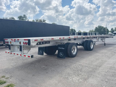 Flatbed trailer showing dual rear axles and wheel fenders with black Great Dane mud flaps, white reflective tape, and a long aluminum deck.