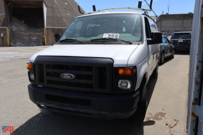 Ford E-150 cargo van front view showing black grille, headlights, and bumper. Vehicle is white with visible windshield tag and side mirrors.