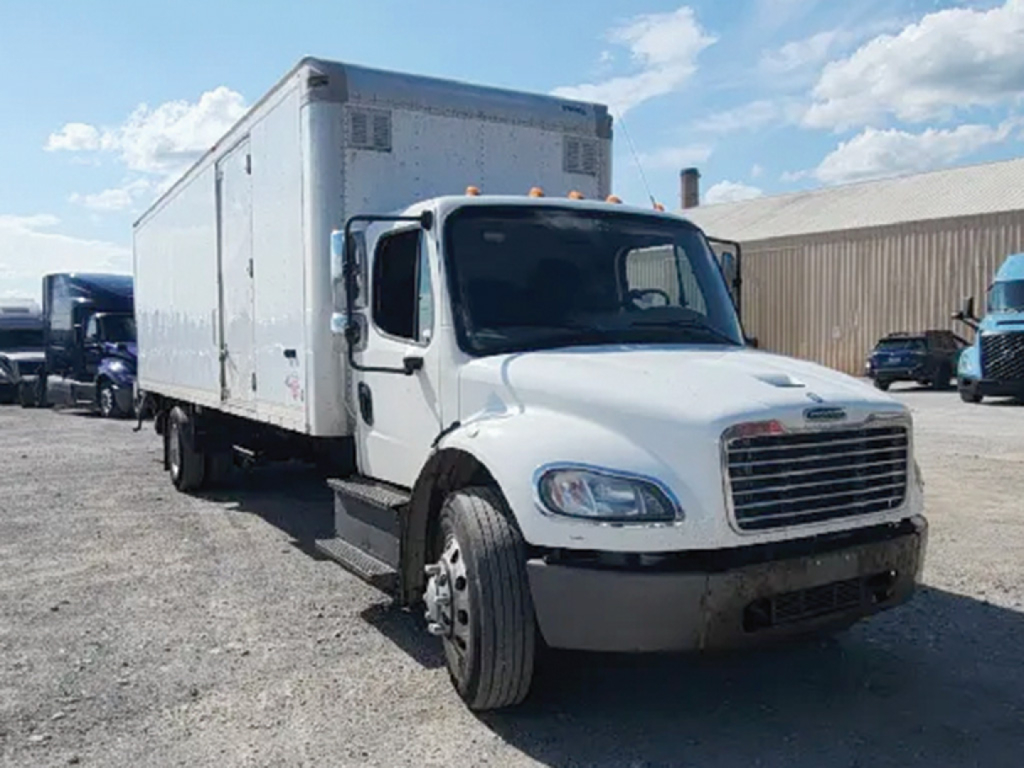 Freightliner M2 106 business class conventional daycab with box truck body in a gravel lot showing front grille and cab details.