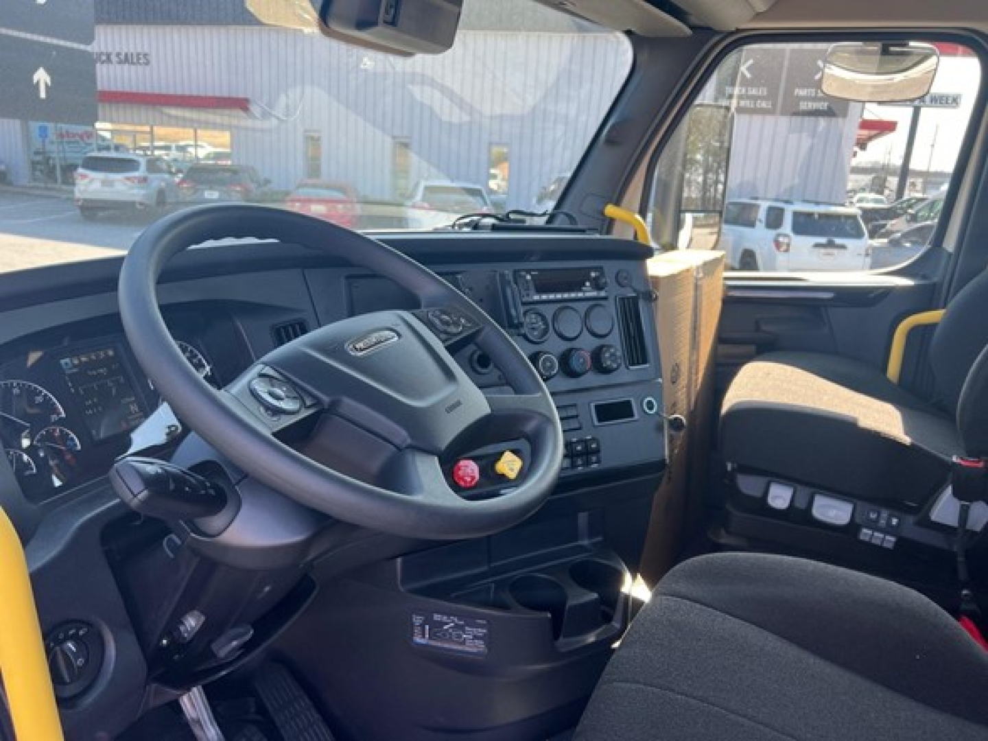 Freightliner Cascadia 116 cockpit with steering wheel, dashboard controls, and driver seat visible.