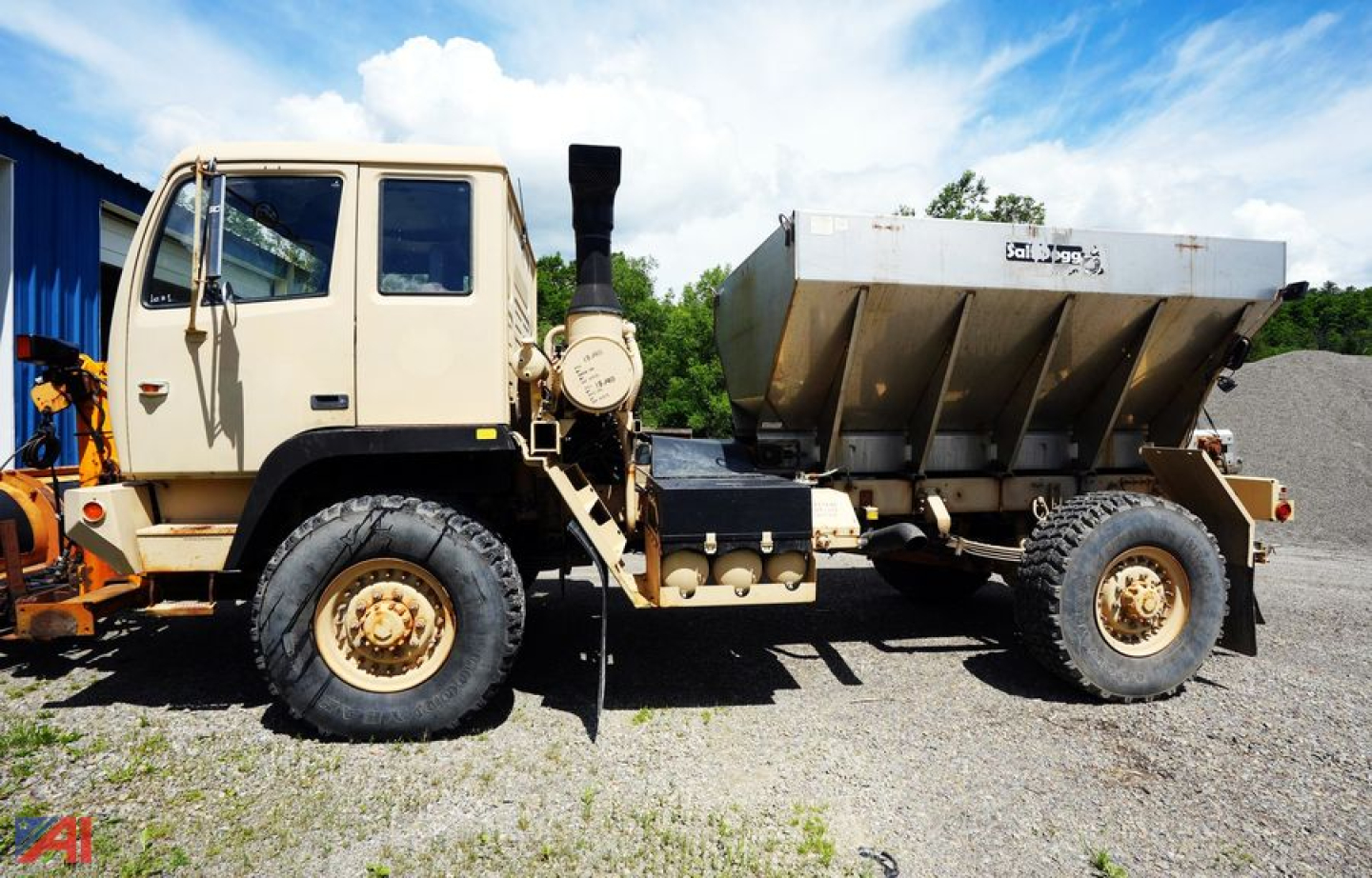 Military plow and spreader truck side view with beige cab and large silver hopper.