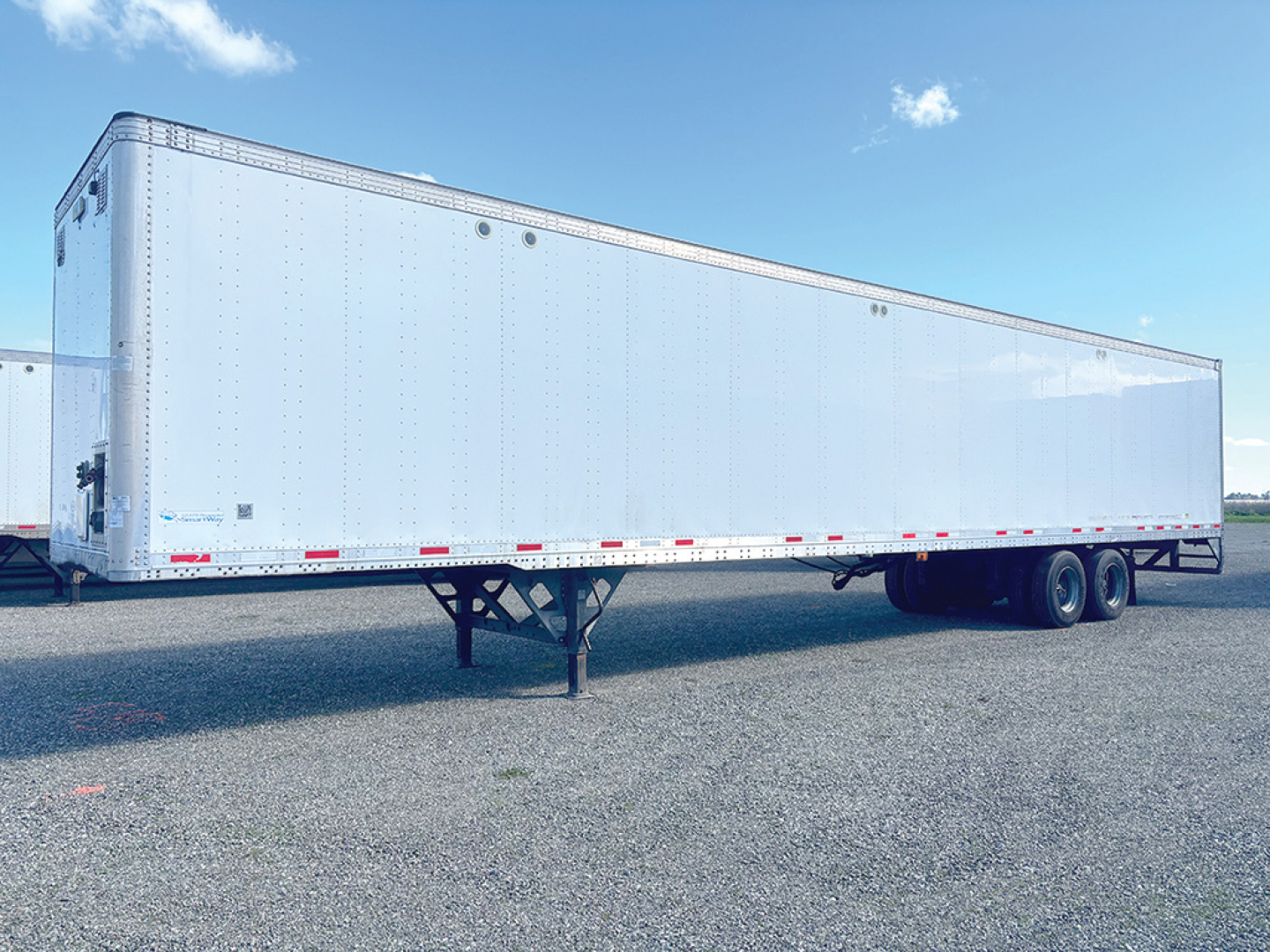 Trailer side view showing aluminum van trailer with landing gear and tandem axle, no text visible on body.