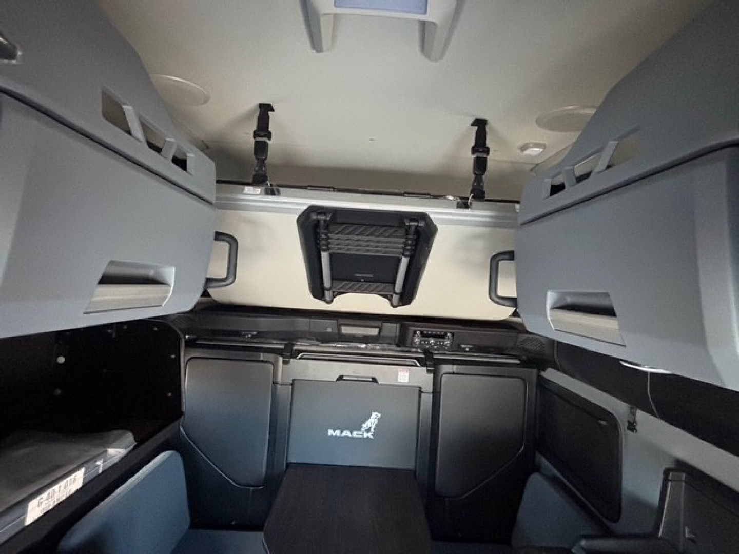 Cab interior of a new Mack PR64T76H sleeper truck showing storage compartments and overhead cabinets.