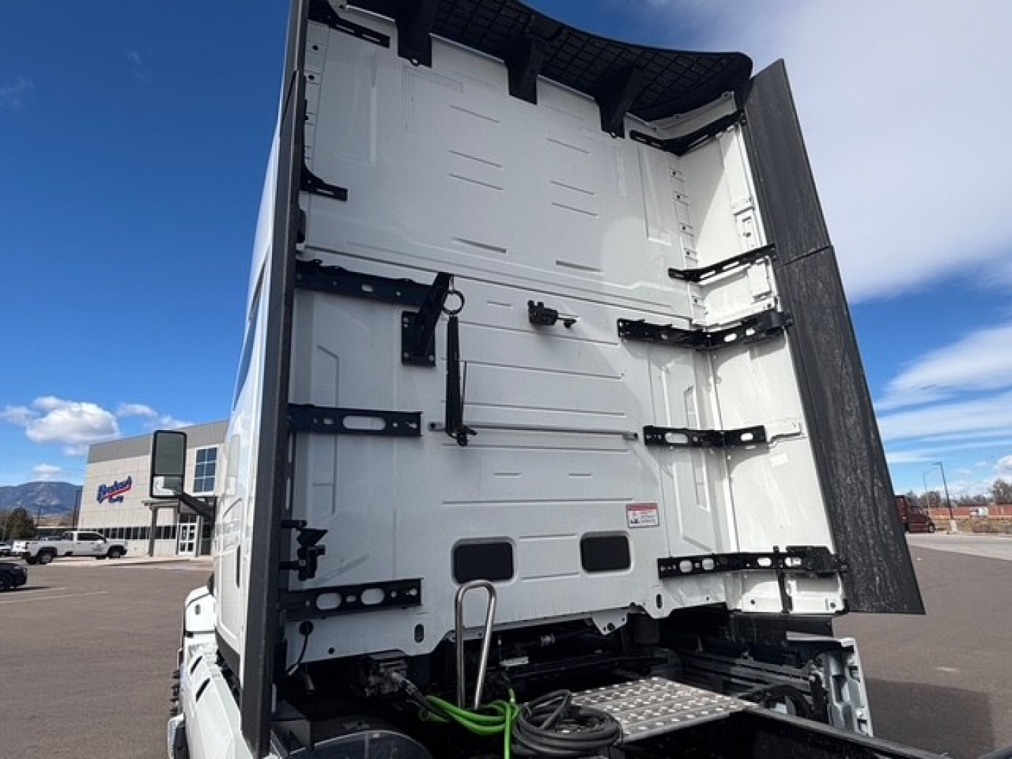 Mack PR64T76H cab interior showing rear tractor sleeper area with white metal walls, black hinges, and a folded tarp/curtain at the back.