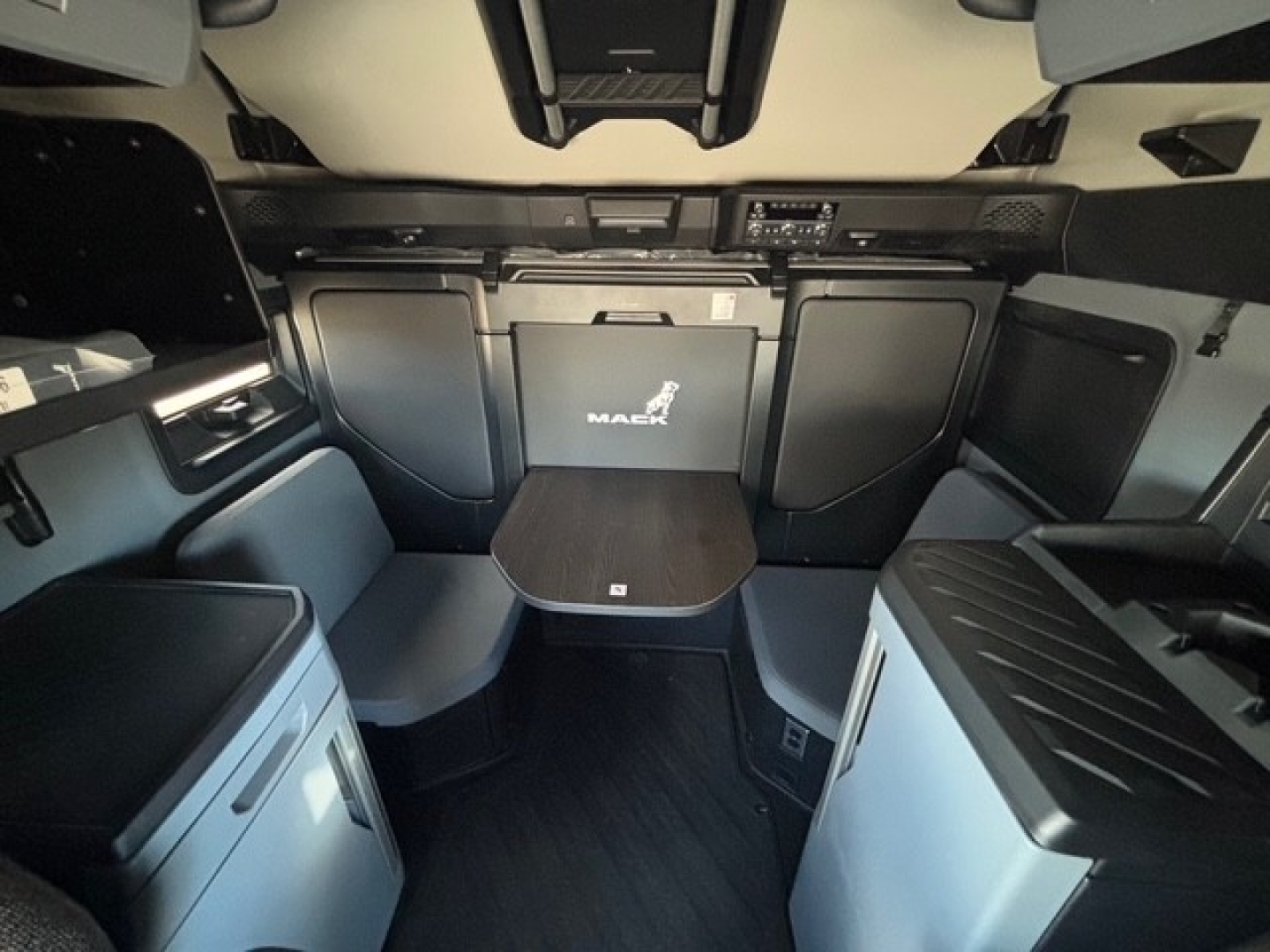 Mack PR64T76H truck cabin interior showing bench seating, table, and storage compartments in a new conventional sleeper.