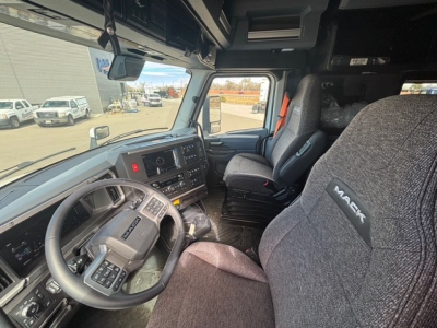 Truck cab interior of a 2026 Mack PR64T76H showing steering wheel, dashboard, and seating. Visible elements include Mack-branded seats, driver controls, and a spacious sleeper area.