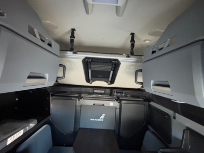 Cab interior of a new Mack PR64T76H sleeper truck showing storage compartments and overhead cabinets.