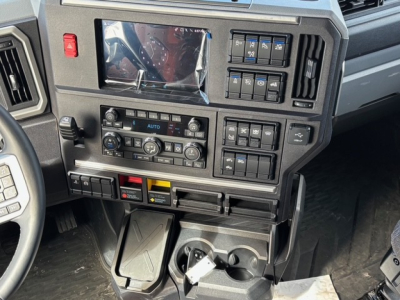 Dashboard of a 2026 Mack PR64T76H truck showing control panels, climate controls, and switches with a small display screen, cup holders, and gear area.